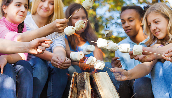teens hold marshmallow sticks on bonfire together
